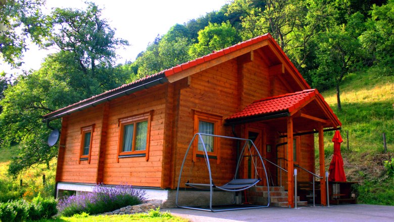 Ferienhaus Brandalm, © zVg Ein Holzferienhaus mit rotem Dach in einer grünen, bewaldeten Umgebung.