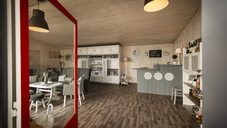 Innenansicht eines gem&uuml;tlichen Caf&eacute;s mit Holzboden, wei&szlig;en M&ouml;beln und dekorativen Elementen.