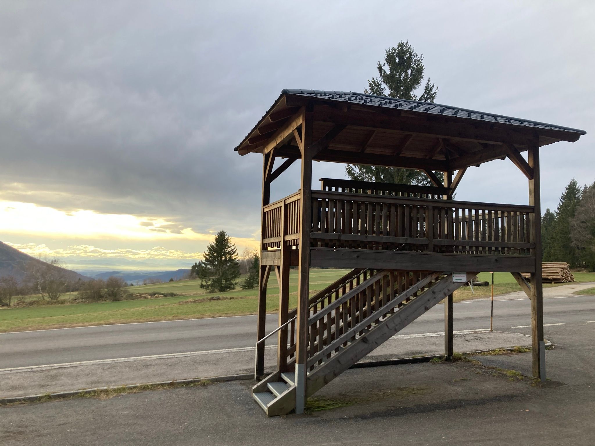 Holzaussichtsplattform mit Blick auf eine Landschaft und bewölkten Himmel.
