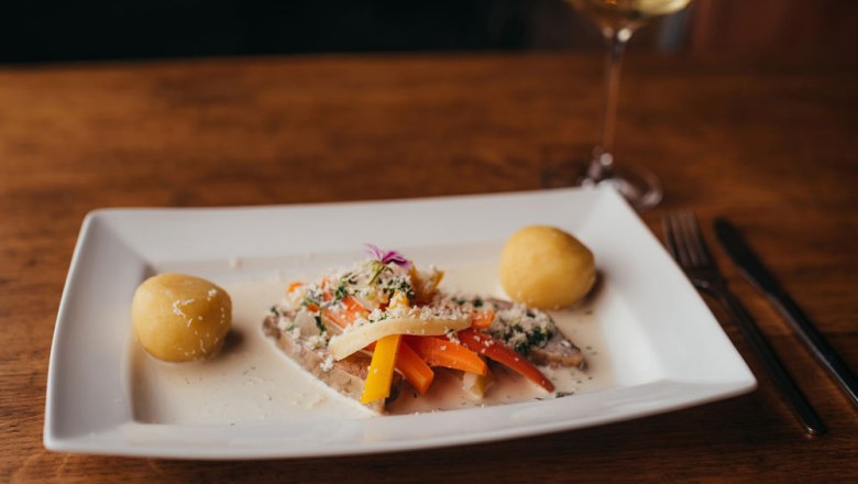 Ein Teller mit Krenfleisch, Wurzelgemüse und Knödeln auf einem Holztisch.