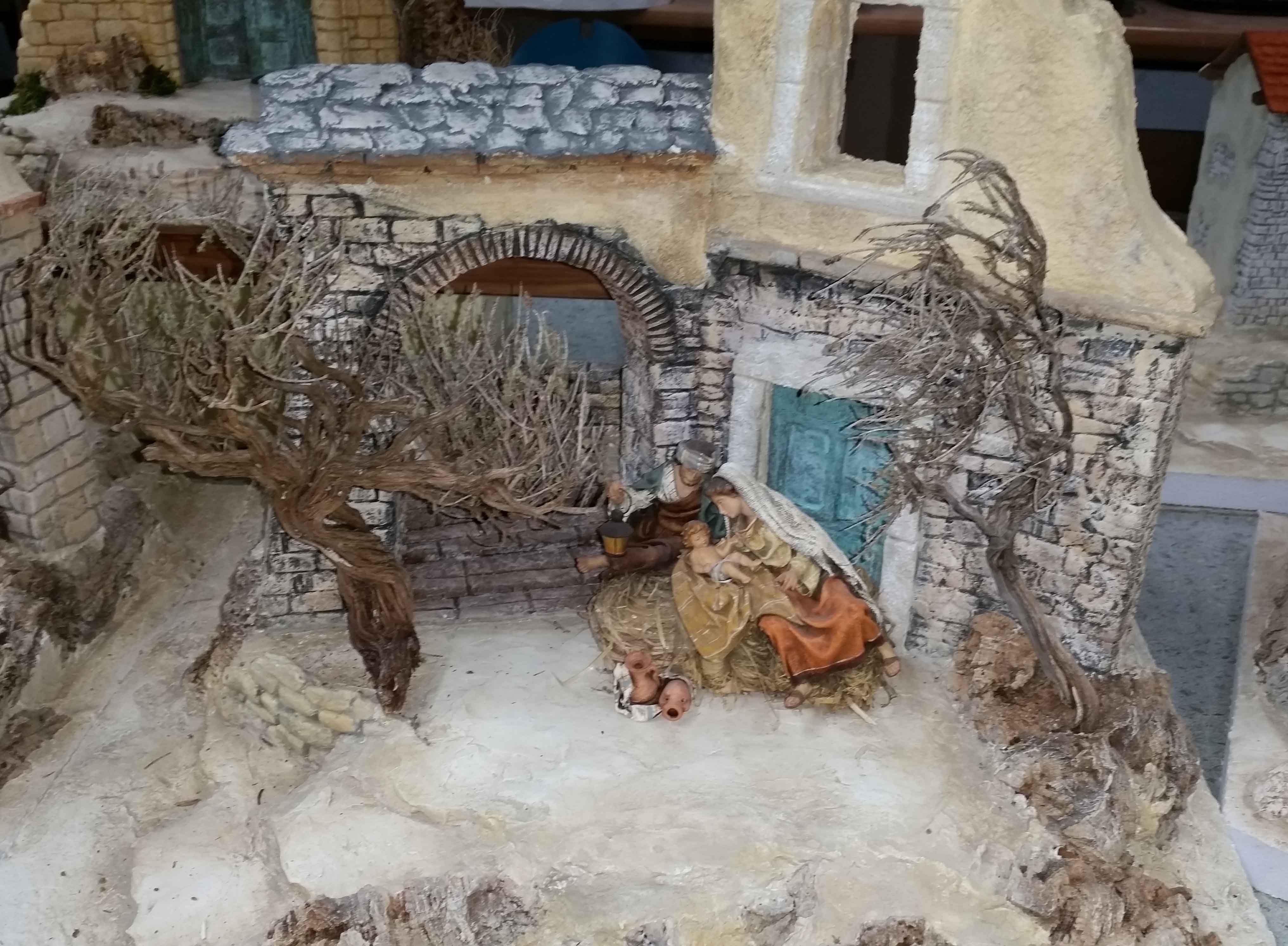 Orientalische Krippenszene mit Figuren unter einem Torbogen, umgeben von Bäumen und Gebäuden.