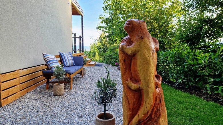 Gartenbereich mit Holzskulptur und Sitzbank beim Chalet Salamander.
