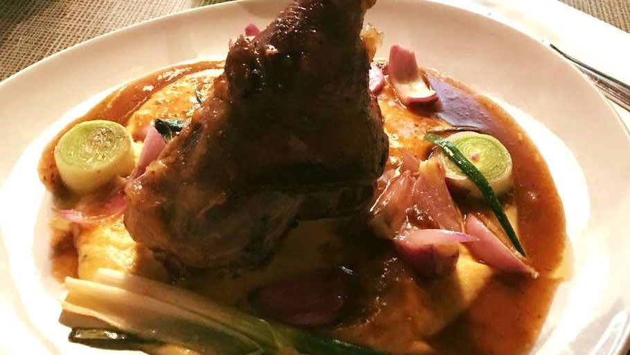 Ein Teller mit einem Fleischgericht, serviert auf Kartoffelpüree mit einer braunen Soße und Gemüse.