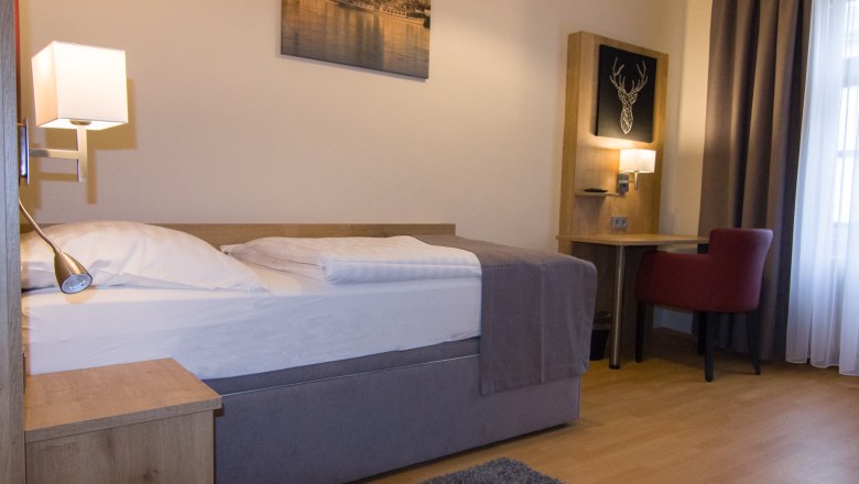 Einzelzimmer mit Bett, Schreibtisch und rotem Stuhl.