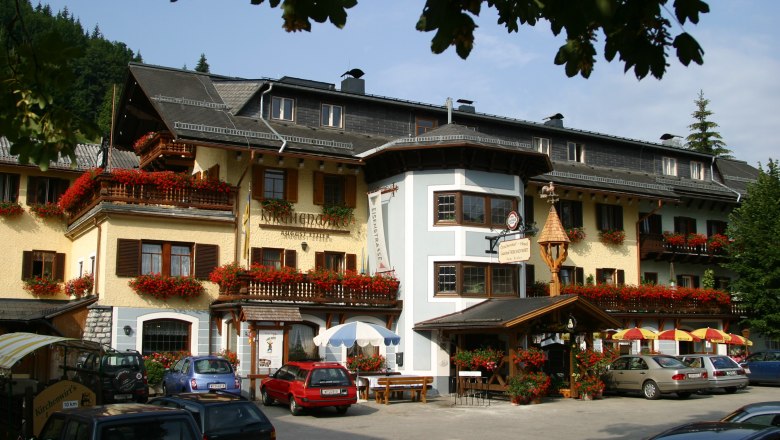 Ein traditionelles Gasthaus mit blumengeschmückten Balkonen und geparkten Autos davor.