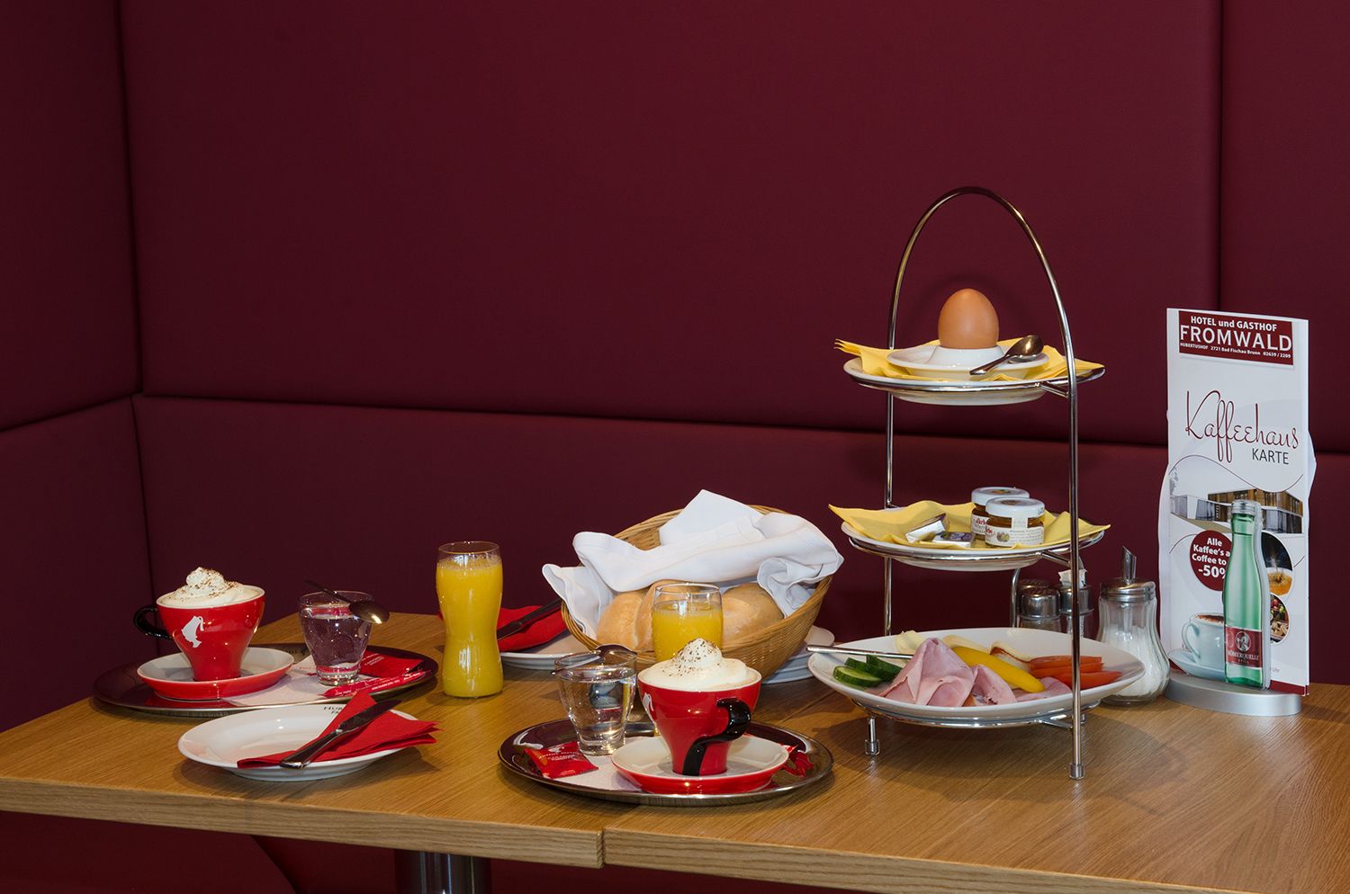 Frühstückstisch mit Kaffee, Orangensaft, Brötchen und Etagere mit Ei und Aufschnitt.