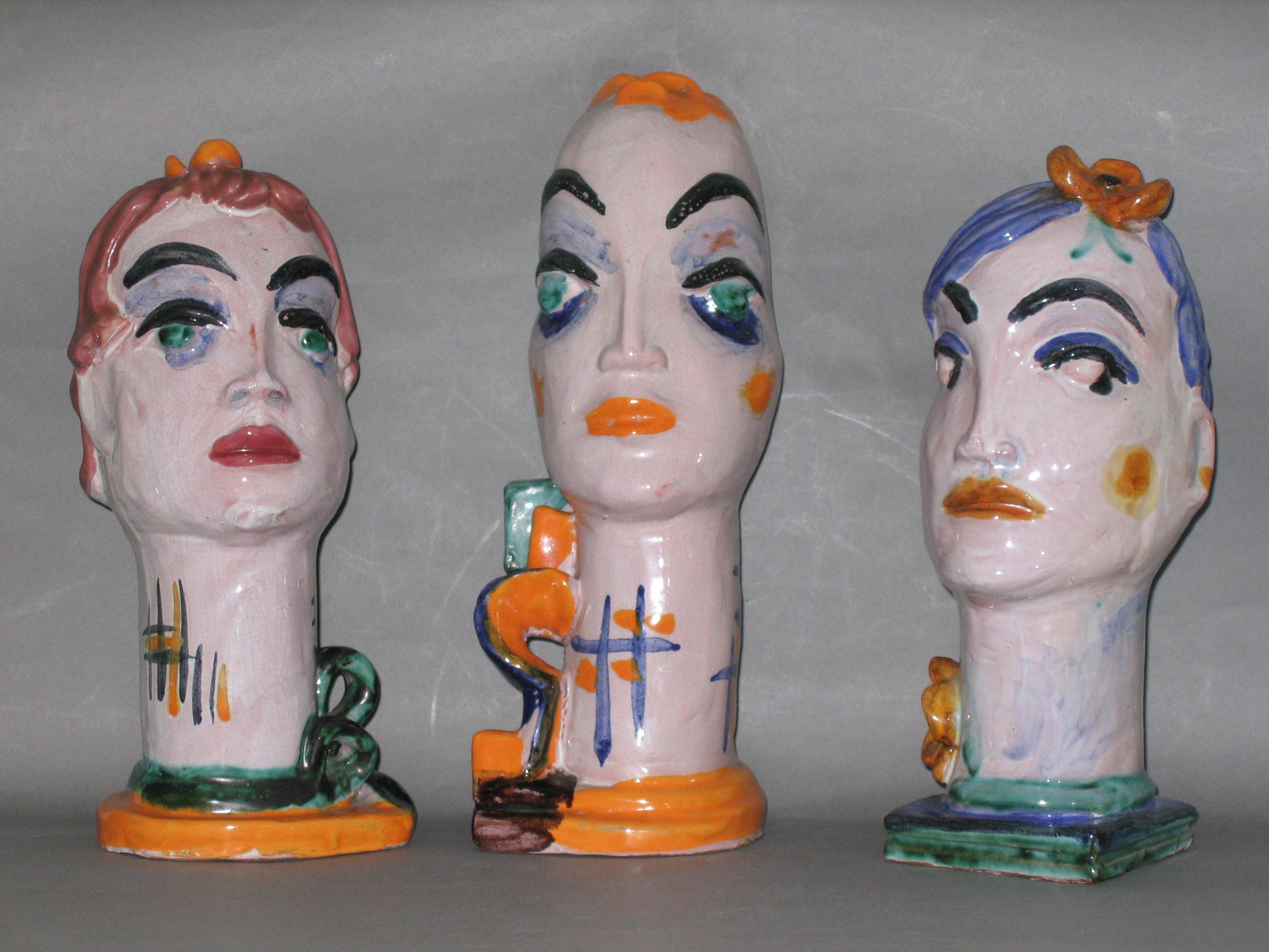 Drei bunte Keramikbüsten mit abstrakten Gesichtern auf grauem Hintergrund.