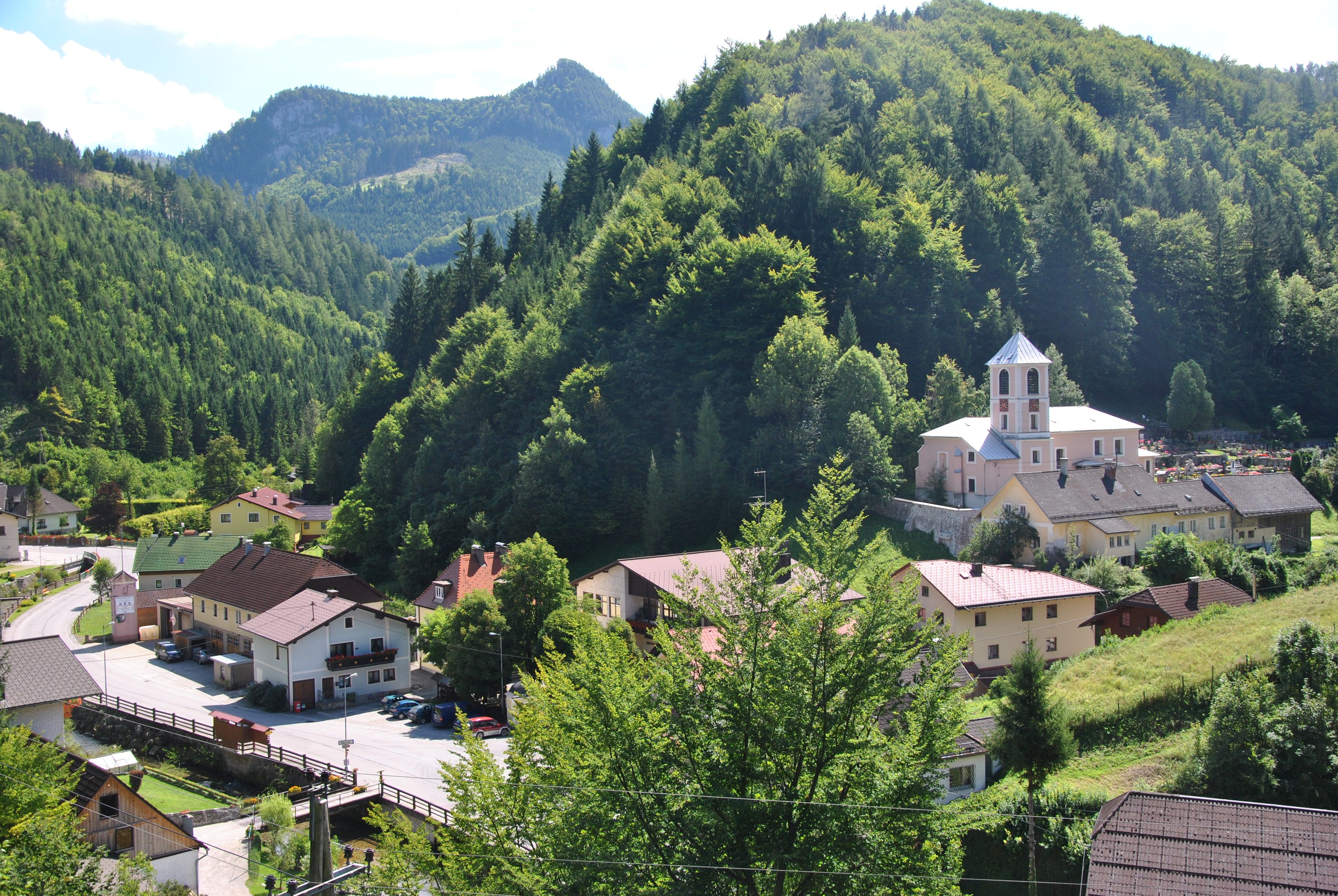 Kleines Dorf in einer grünen Berglandschaft mit Kirche und Häusern.