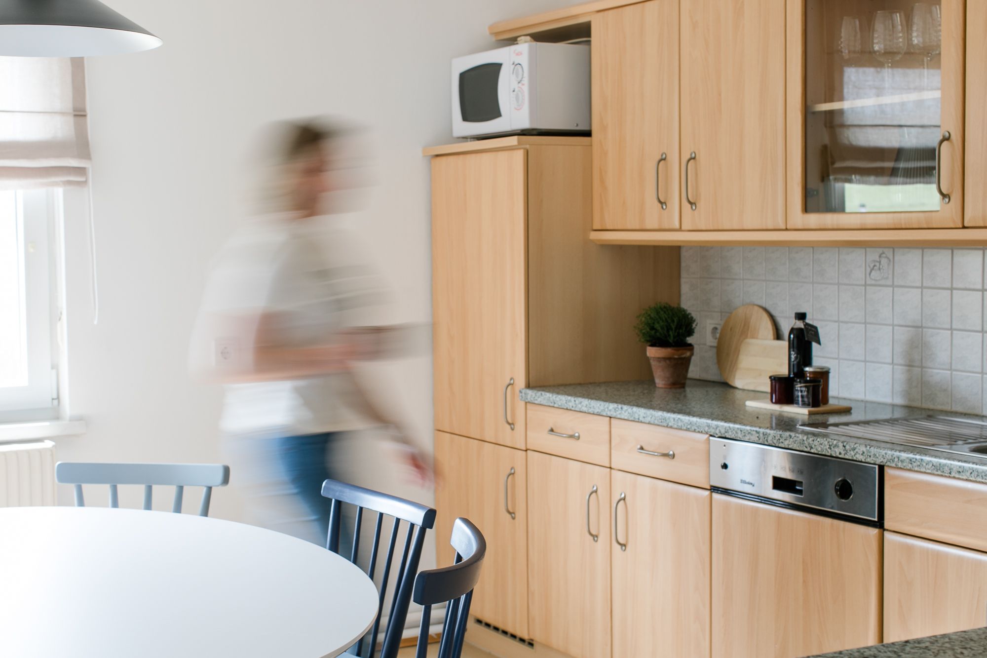 Moderne Küche mit Holzmöbeln und einer Person in Bewegung.