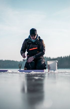 Ein Fischer sitzt konzentriert auf dem glitzernden Eis des Stausees Ottenstein und bereitet seine Angelausrüstung vor. Die ruhige Winterlandschaft, umgeben von schneebedeckten Bäumen, schafft eine friedliche Atmosphäre, die zum Entspannen einlädt. Hier, in der Stille der Natur, wird das Eisfischen zu einem unvergesslichen Erlebnis.