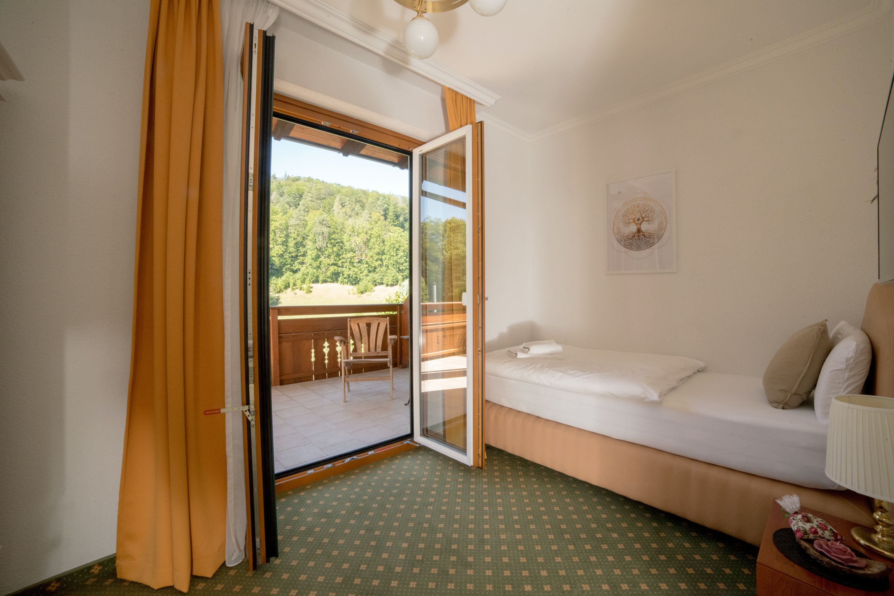 Einzelzimmer mit Balkon, Einzelbett, geöffnete Balkontür, Blick auf grüne Landschaft.