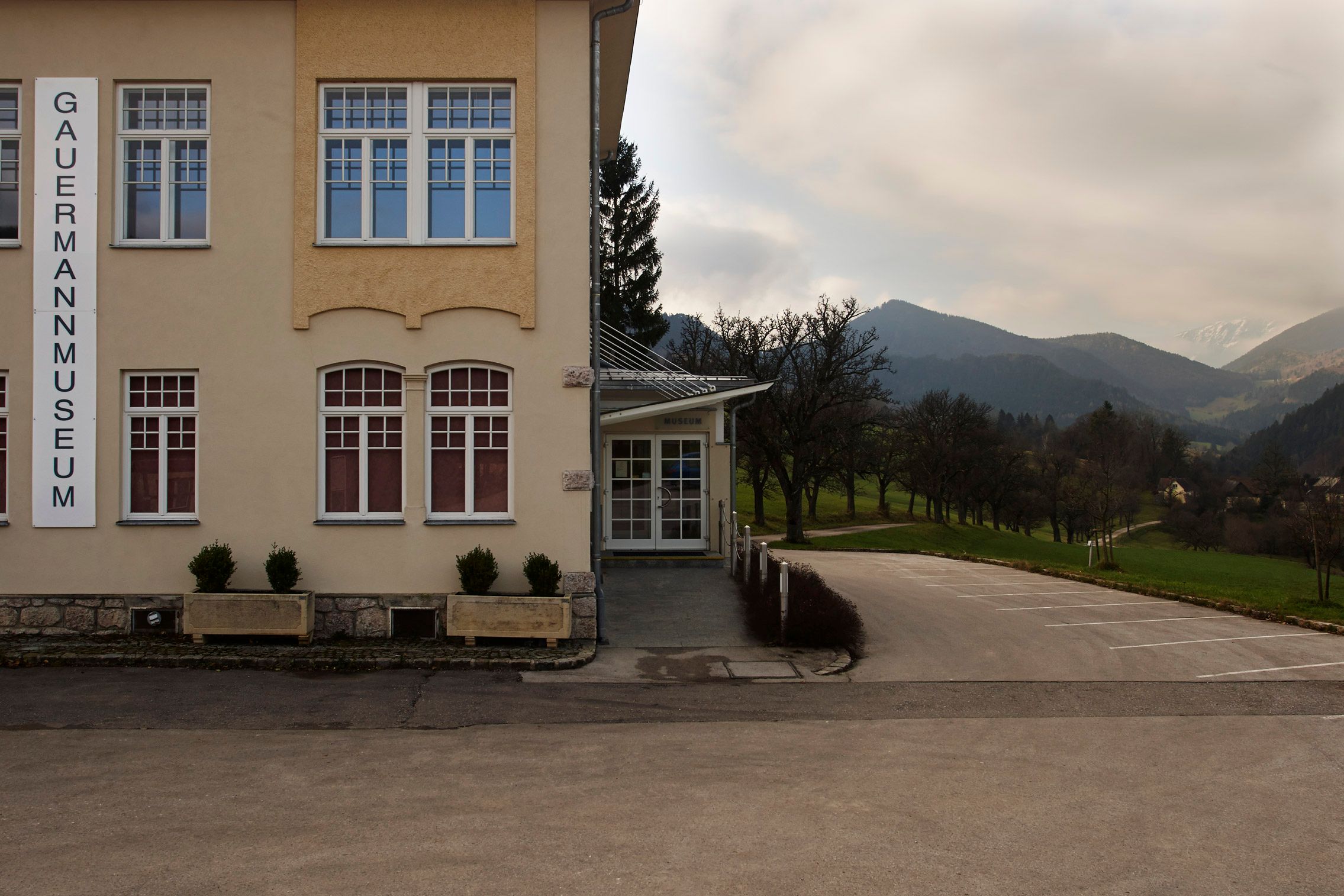 Außenansicht des Gauermannmuseums in Miesenbach mit Berglandschaft im Hintergrund.