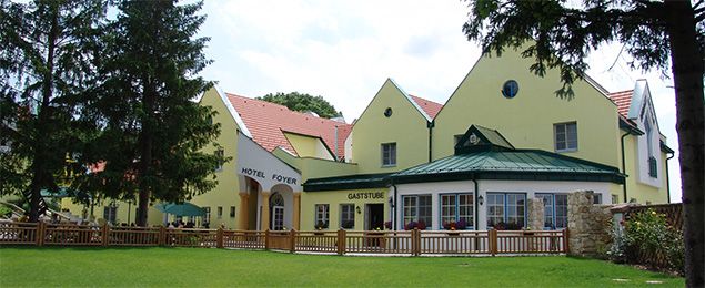 Gelbes Gebäude mit Hotel und Gaststube, umgeben von Bäumen und Rasen.