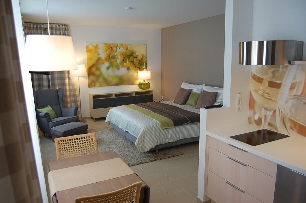 Modernes Apartment mit Bett, Sessel, Tisch und Küchenzeile.