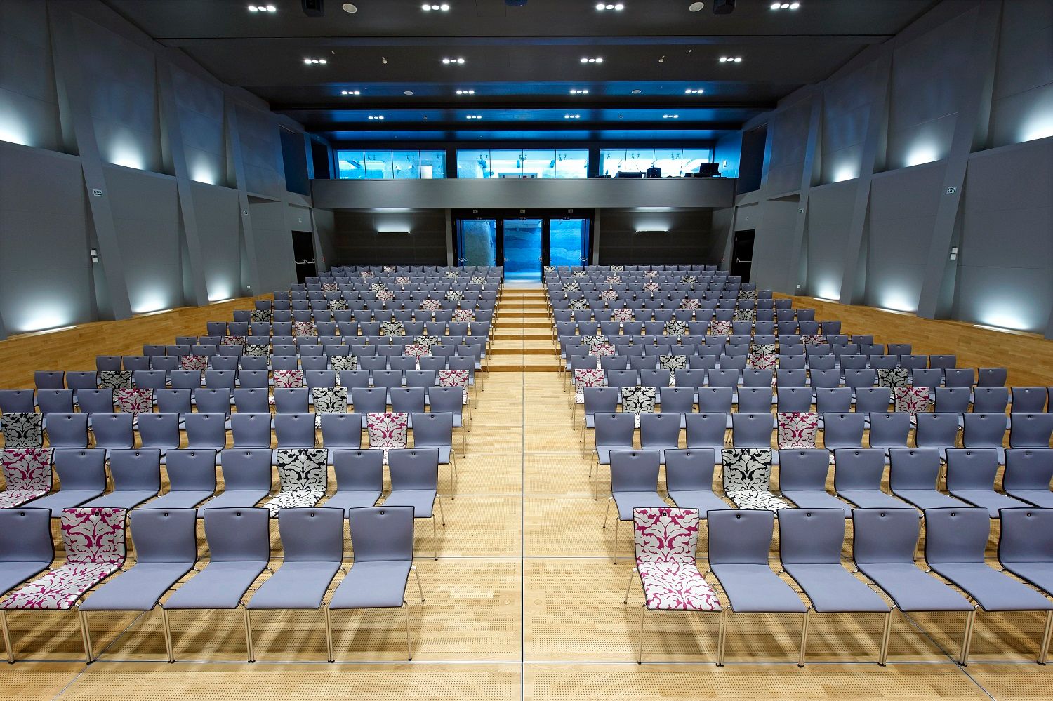 Moderner Saal mit vielen leeren Stuhlreihen, einige mit gemusterten Bezügen.