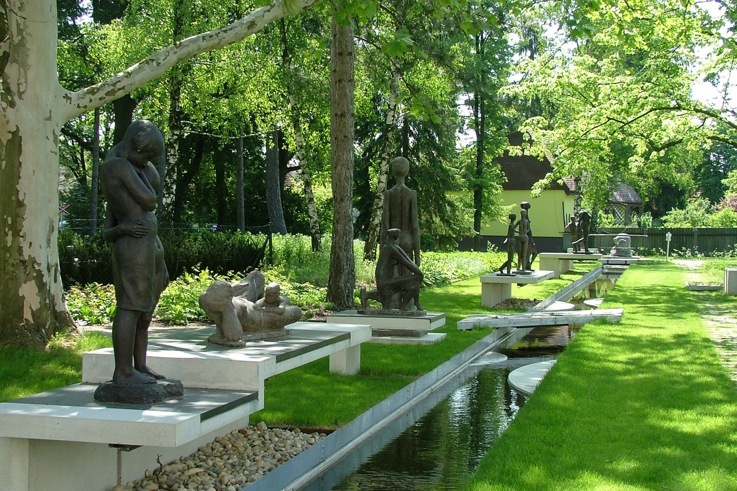 Skulpturen im Freien in einem grünen Park mit Bäumen und einem Wasserlauf.