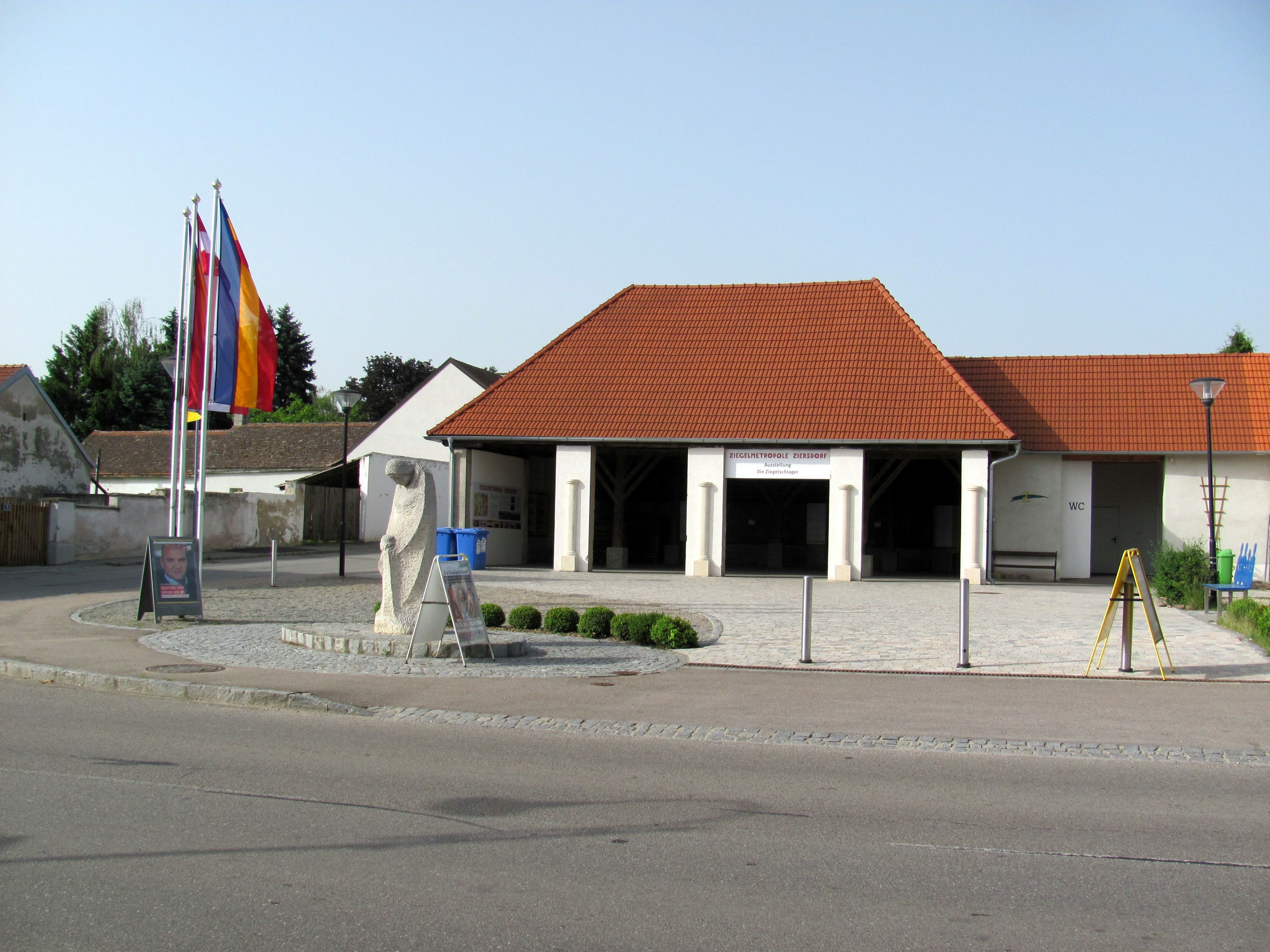 Außenansicht des Ziegelmuseums in Ziersdorf mit roten Dachziegeln und Flaggen.