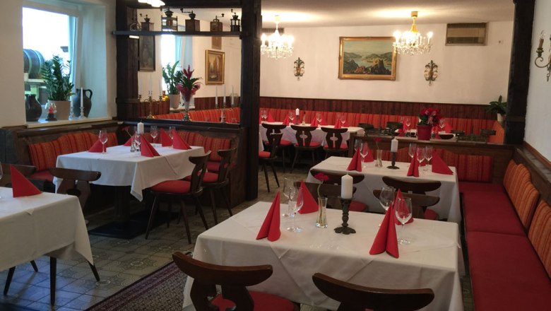 Innenansicht eines traditionellen Wirtshauses mit gedeckten Tischen und roten St&uuml;hlen.
