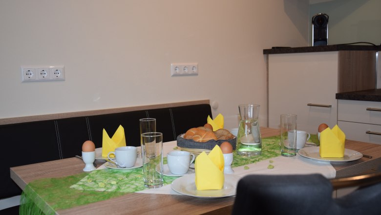 Frühstückstisch mit Brötchen, Eiern, Tassen und gelben Servietten.