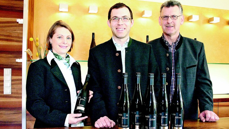 Drei Personen stehen hinter einem Tisch mit Weinflaschen im Weingut Holzer.