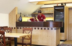 Zwei Personen hinter einer Holzausschank in einem rustikalen Raum.