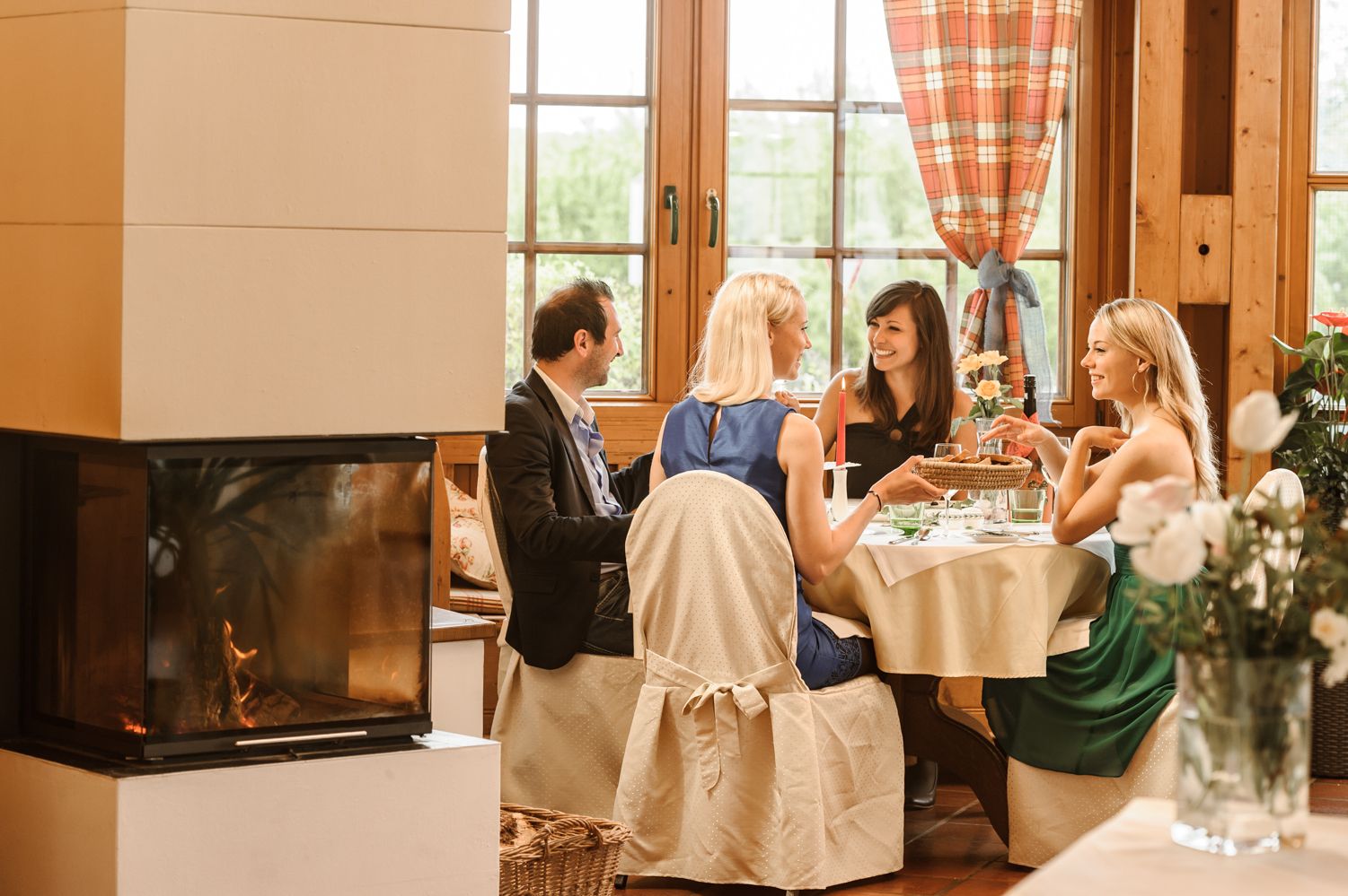 Vier Personen sitzen an einem Tisch in einem gemütlichen Wintergarten mit Kamin.