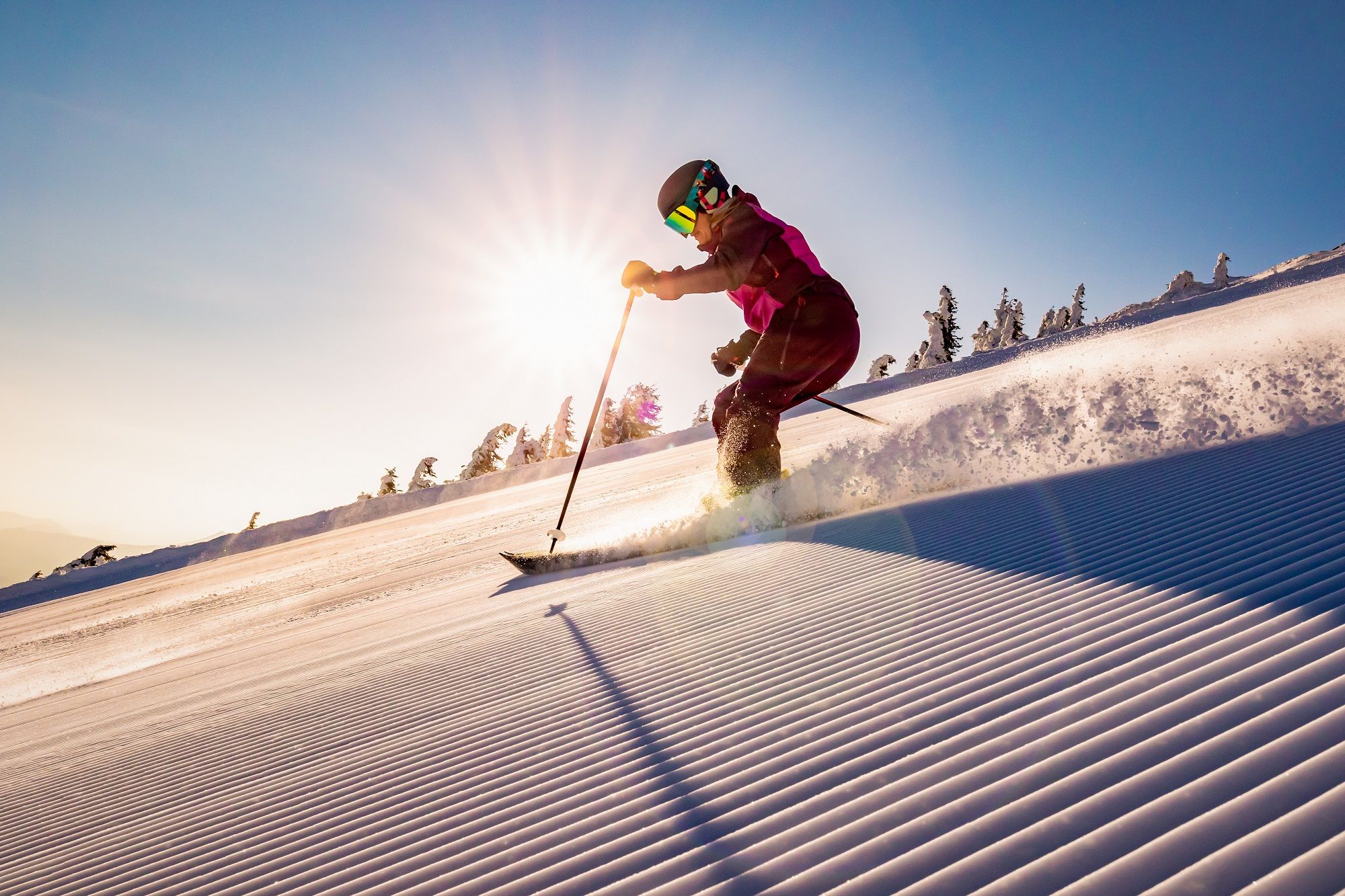 Skifahrer fährt bei Sonnenaufgang auf einer frisch präparierten Piste bergab.