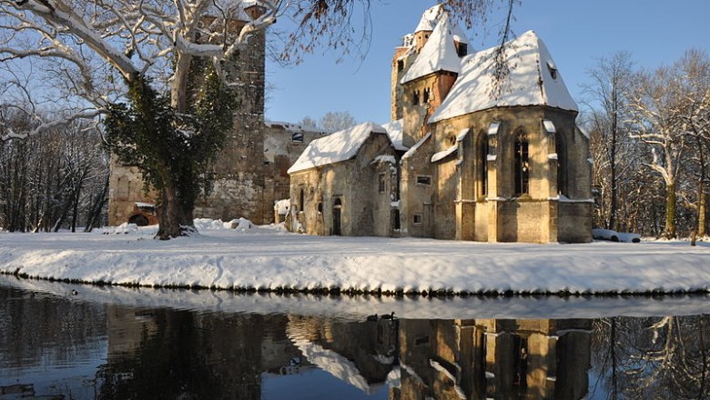 Winterliche Schlossruine Pottendorf mit Schnee und Spiegelung im Wasser.