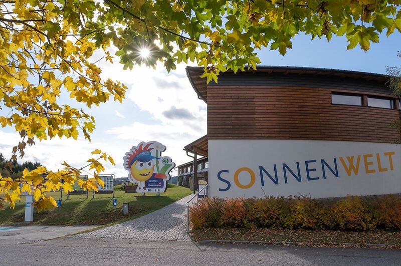 Eingang zur SONNENWELT Großschönau mit herbstlichen Bäumen und Sonnenschein.