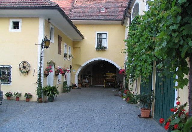 Innenhof eines traditionellen Winzerhofs mit gelben Wänden, Blumen und Weinreben.