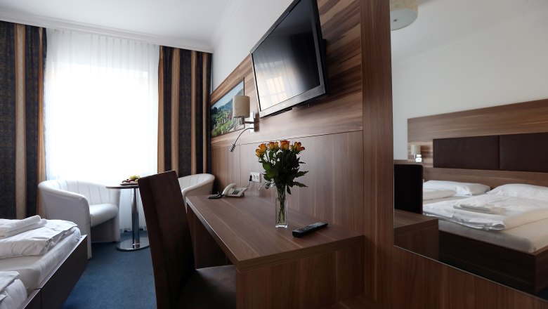 Modern eingerichtetes Hotelzimmer mit Doppelbett, Schreibtisch, Flachbildfernseher und Blumenstrau&szlig;.