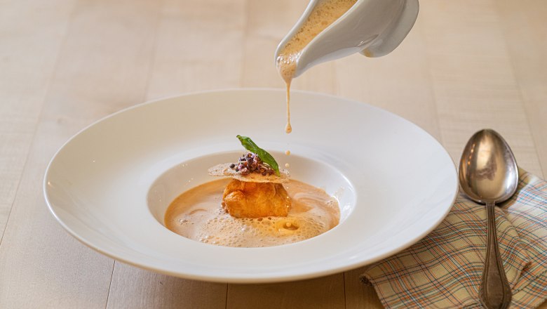 Krebssuppe wird in einen Teller gegossen, dekoriert mit einer Teigkugel und Kr&auml;utern.