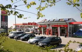 Tankstelle mit AVIA-Logo und mehreren geparkten Autos im Vordergrund.