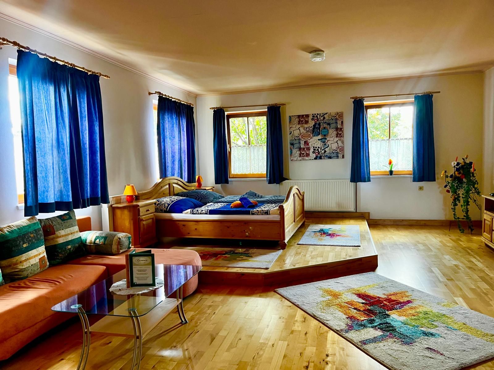 Gemütliches Zimmer mit Holzboden, Doppelbett, Sofa und blauen Vorhängen.