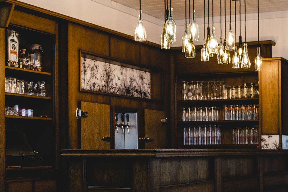 Eine gemütliche Bar mit hölzernem Interieur und hängenden Flaschenlampen.