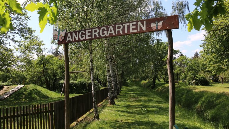 Eingang zu den Angerg&auml;rten mit Holzschild und B&auml;umen im Hintergrund.