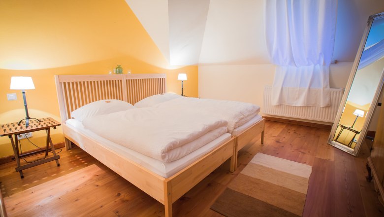 Gem&uuml;tliches Schlafzimmer mit Doppelbett, Holzboden, gelber Wand und gro&szlig;em Spiegel.