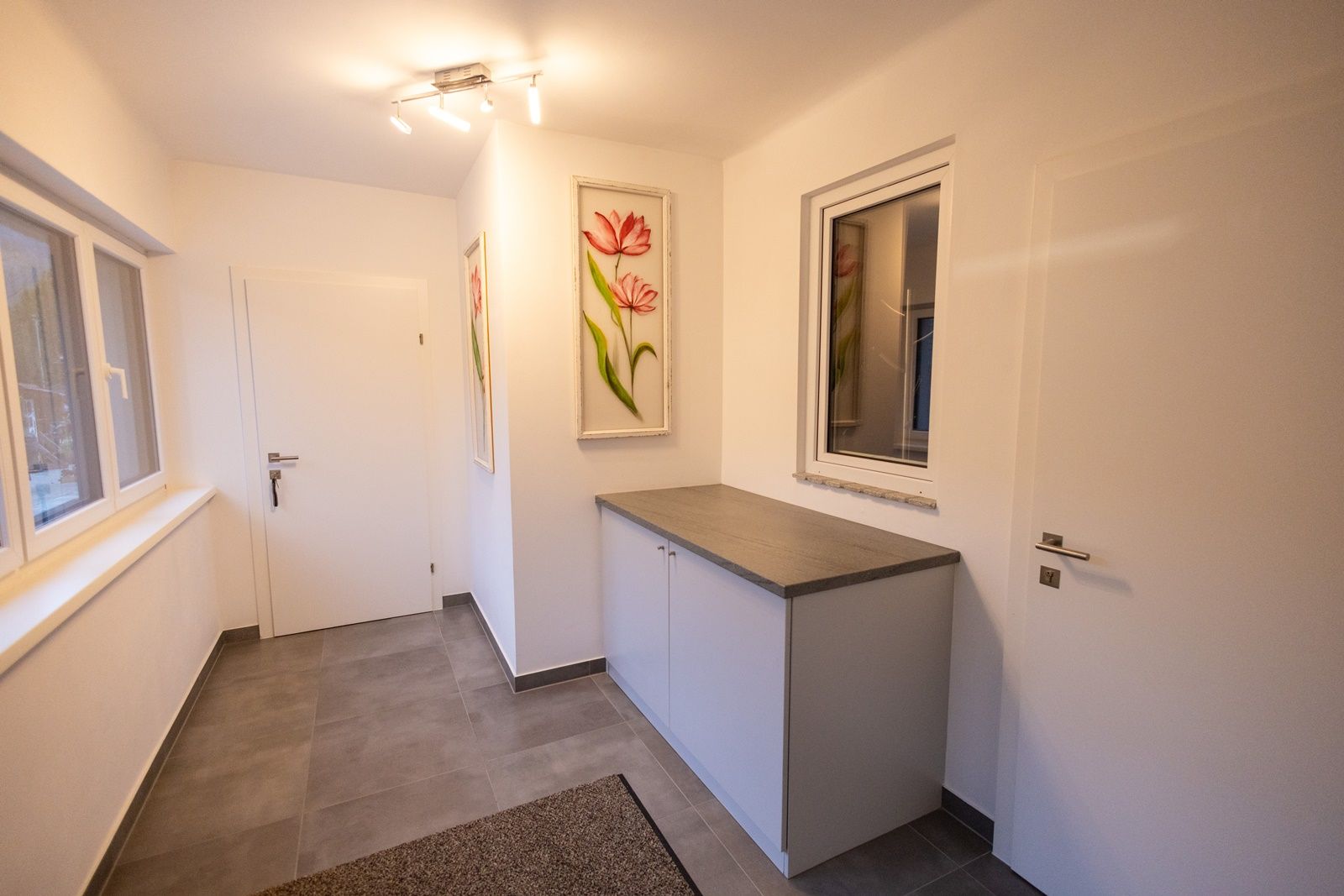 Moderner Vorraum mit weißen Wänden, grauem Boden, einem Schrank und Blumenbildern an der Wand.