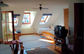 Innenansicht eines gem&uuml;tlichen Dachgeschosszimmers mit Holzm&ouml;beln, zwei Betten, einem Fernseher und Dachfenstern.