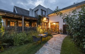 Eingangsbereich des Restaurants Triad, beleuchtet am Abend und mit Terrasse