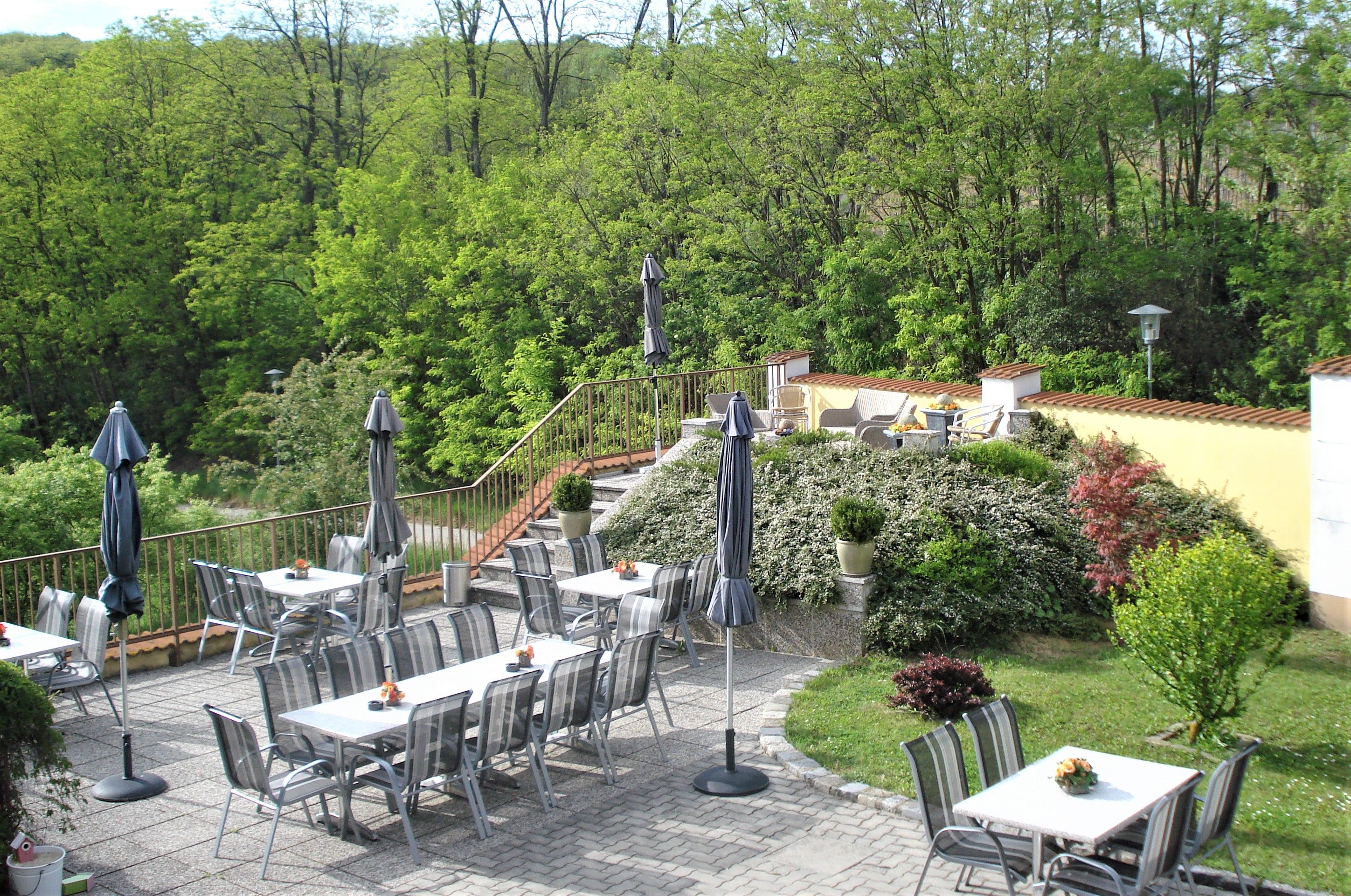 Gästeterrasse mit Tischen, Stühlen und Sonnenschirmen, umgeben von grüner Vegetation.