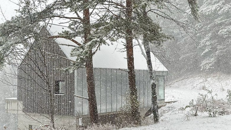 Caspar´s Home im Winter, © Meinrad Hofer Ein modernes Haus im Wald, umgeben von Schnee und Bäumen, während es stark schneit.