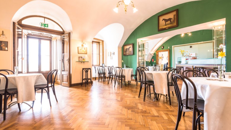 Innenansicht eines eleganten Cafés mit Holzboden, weißen Tischdecken und grüner Wand.