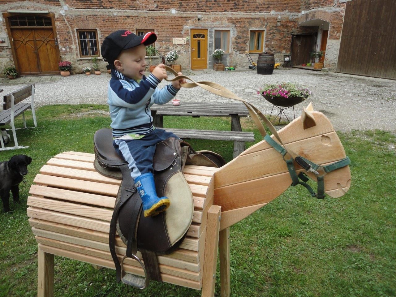Ein Kind sitzt auf einem hölzernen Spielzeugpferd im Freien.