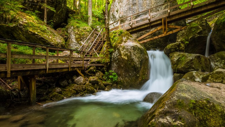 Wasserfall mit Holzbr&uuml;cken und Treppen in einem bewaldeten Gebiet.