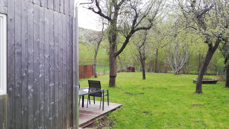 Holzscheune neben Obstgarten mit Tisch und St&uuml;hlen auf Holzterrasse.
