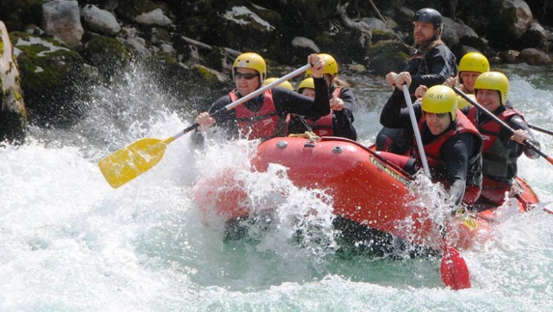Gruppe beim Rafting auf einem Fluss mit gelben Helmen und roten Westen.
