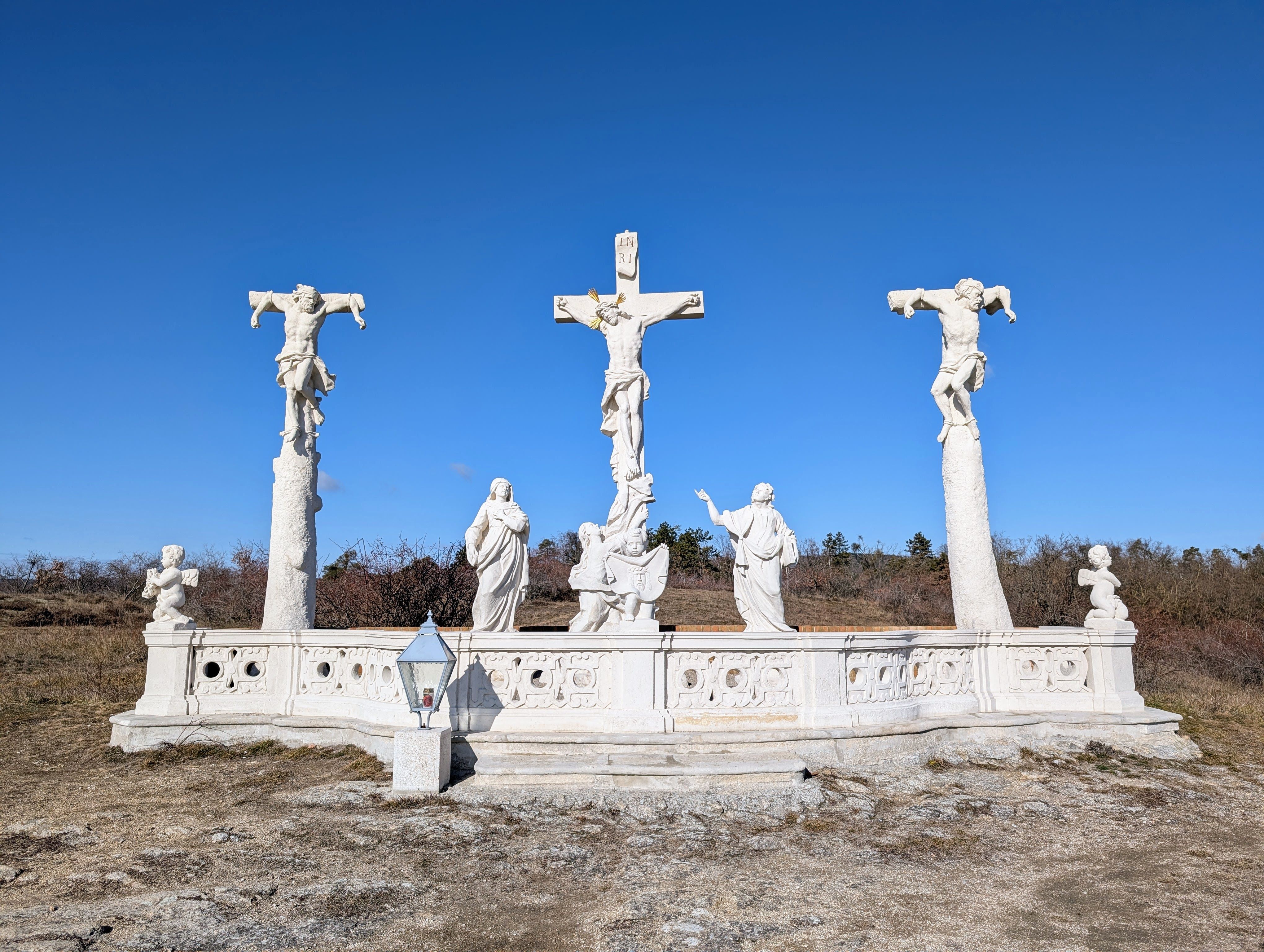 Kalvarienberg mit drei Kreuzen und Statuen vor blauem Himmel.