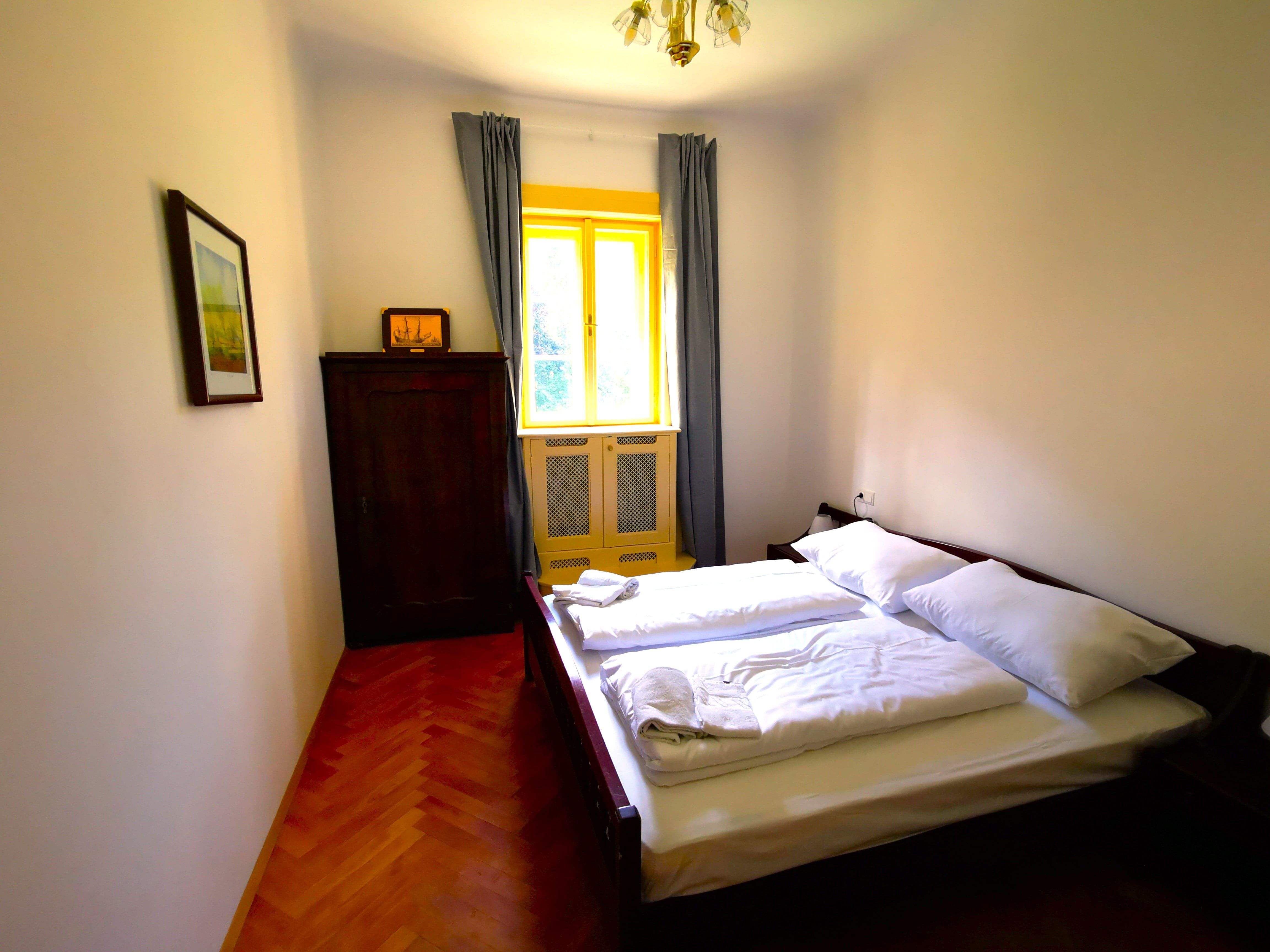 Schlafzimmer mit Doppelbett, Schrank und Fenster mit gelbem Rahmen.