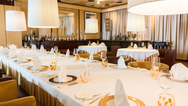 Eleganter Speisesaal mit gedeckten Tischen, weißen Tischdecken und großen Hängelampen.